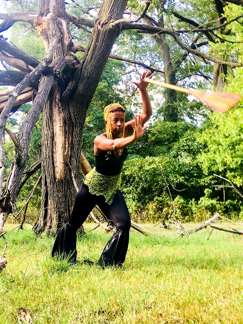 Photo of Donne Lewis dancing with broom in forest