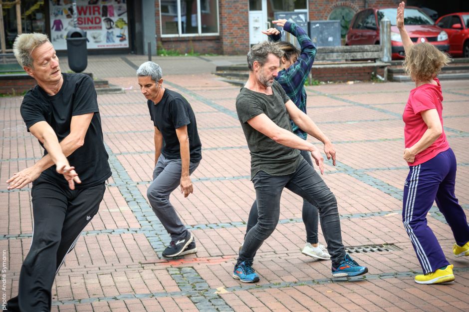 Five dancers outside on brick pavement walk and move in different directions.