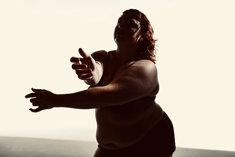 KT in silhouette with her arms crossed and reaching in front of her.