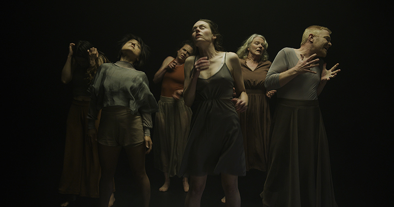 Six people in eerie light against a black background move their heads and gesture in different directions.