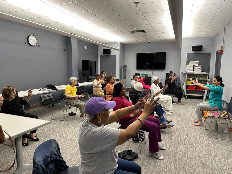 Sloka leads a group of seniors as they lift their arms in front of them. 