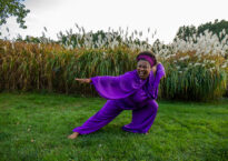 Sydnie does a deep lunge in a purple jumpsuit on grass.