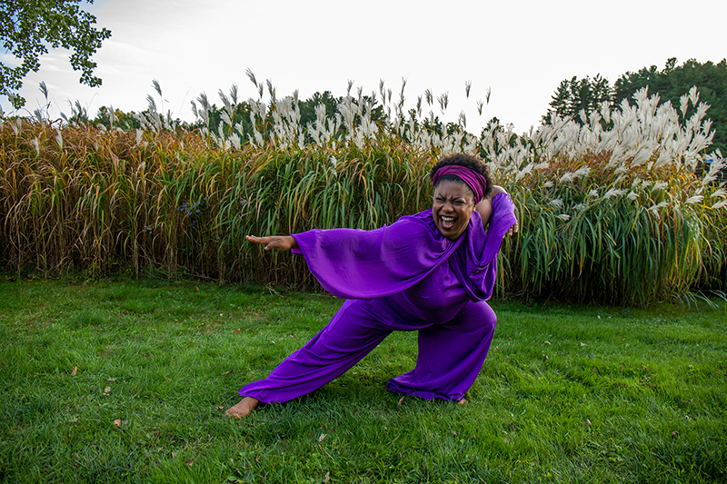 Sydnie does a deep lunge in a purple jumpsuit on grass.