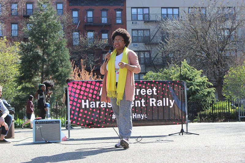 Sydney stands and speaks into a microphone at an event outside.
